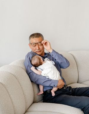 A parent and infant share a tender moment while relaxing together on a light-colored couch.