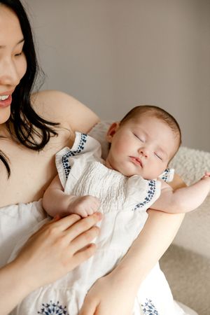 A sleeping baby in white clothing nestled against a cream background in a series of gentle poses.
