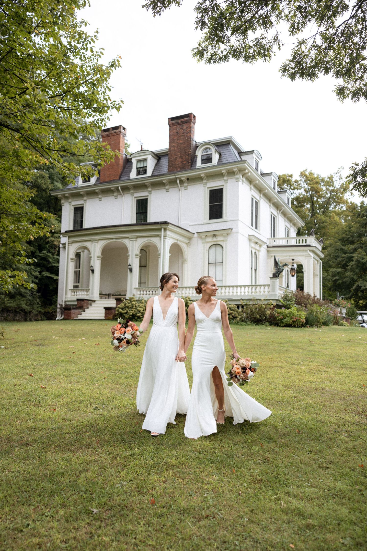 Wedding party poses on the lawn of a grand white historic mansion with Victorian details.
