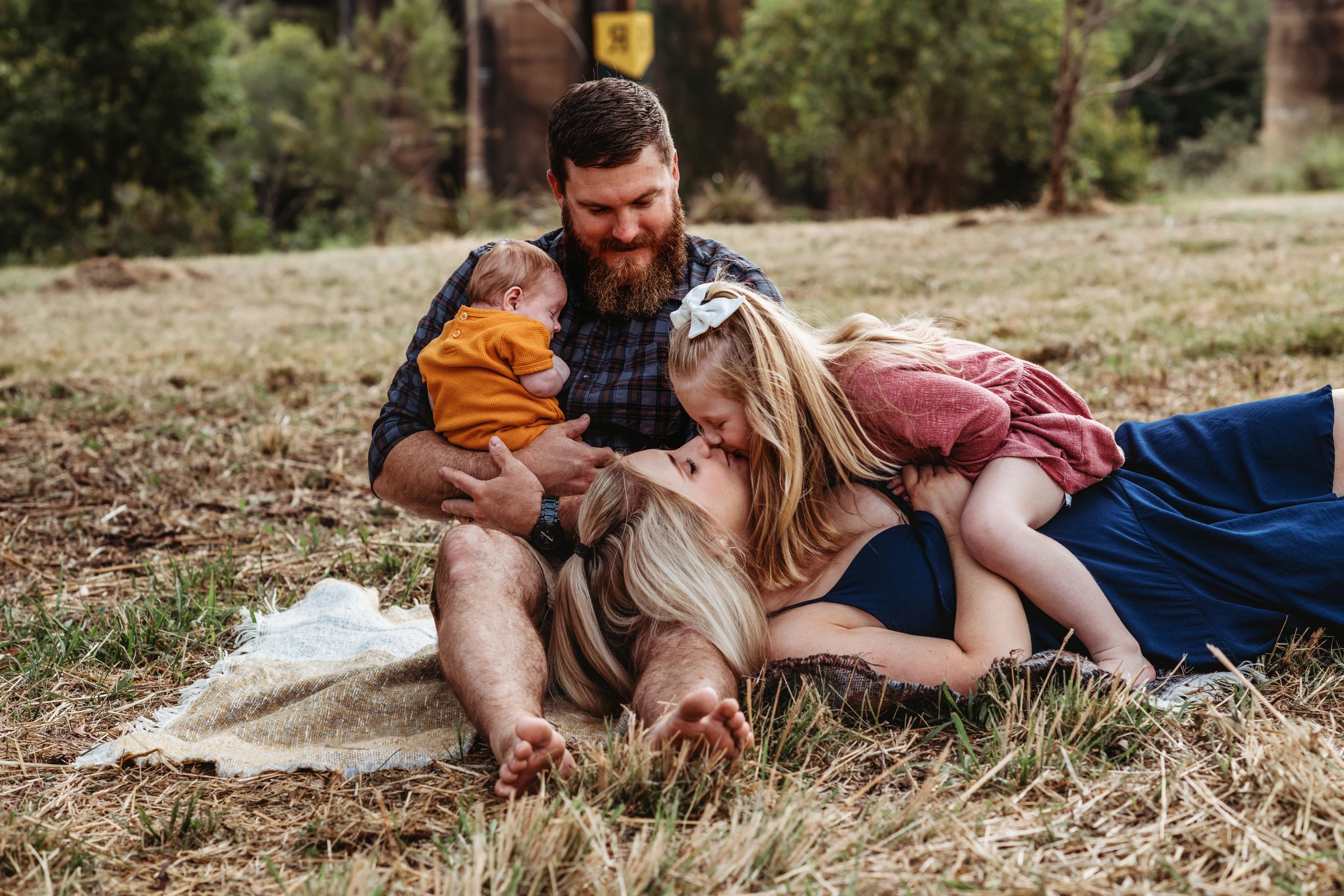 Family relaxing together on blanket in grassy field during outdoor photo session.