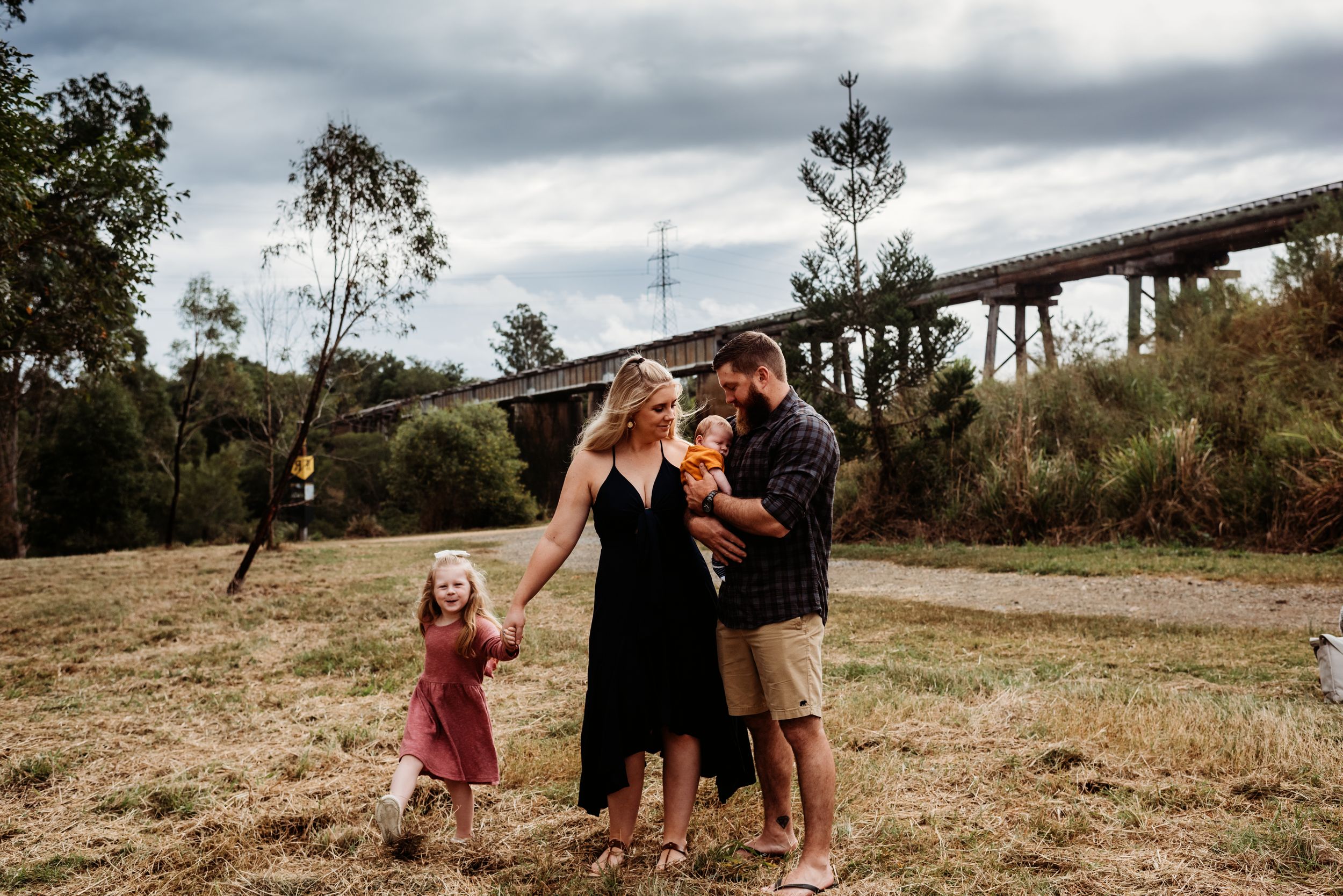 Family enjoying a tender moment together in front of a bridge on an overcast day.