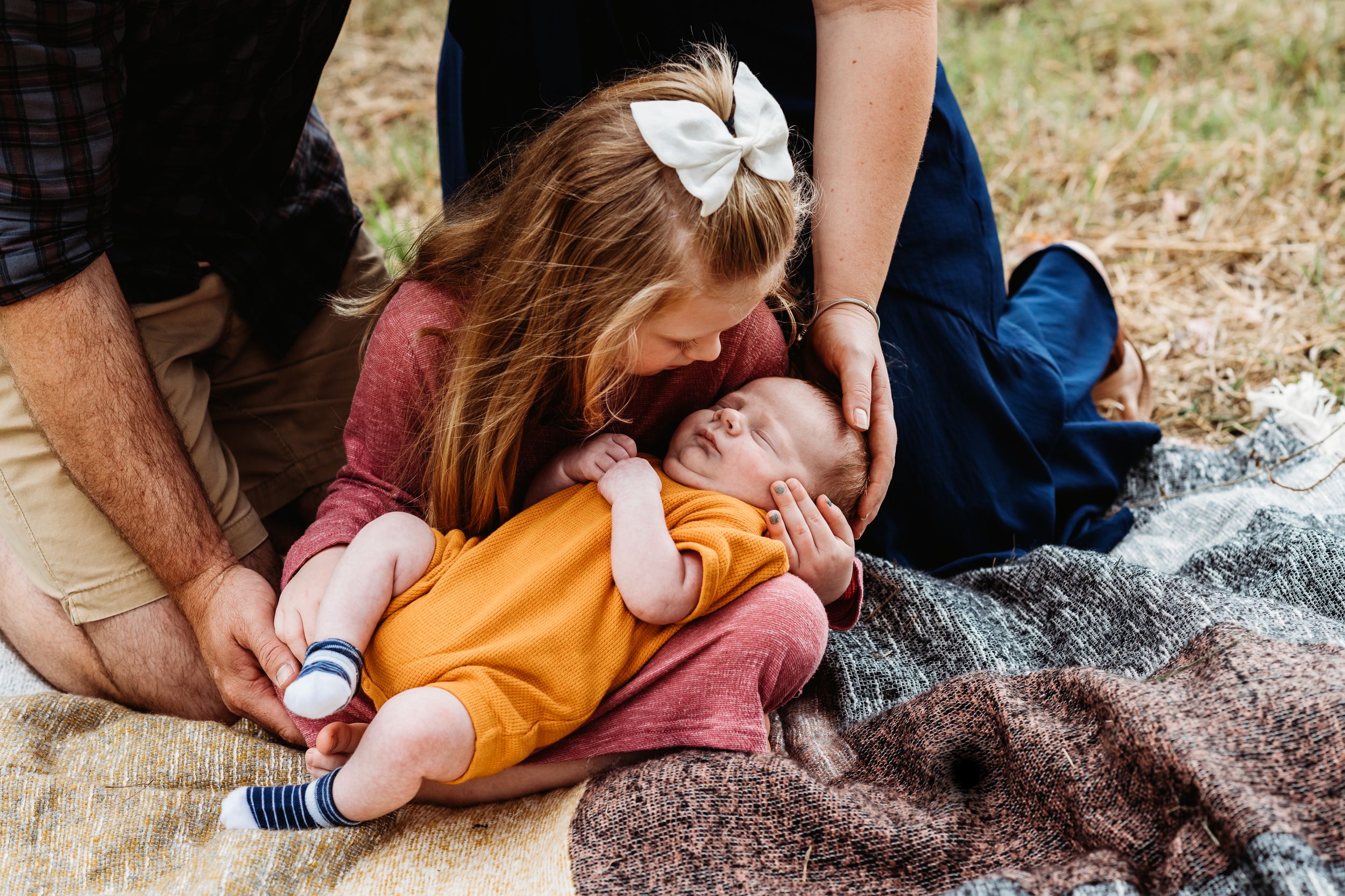 Candid family moment of parents and baby relaxing together on picnic blanket outdoors.