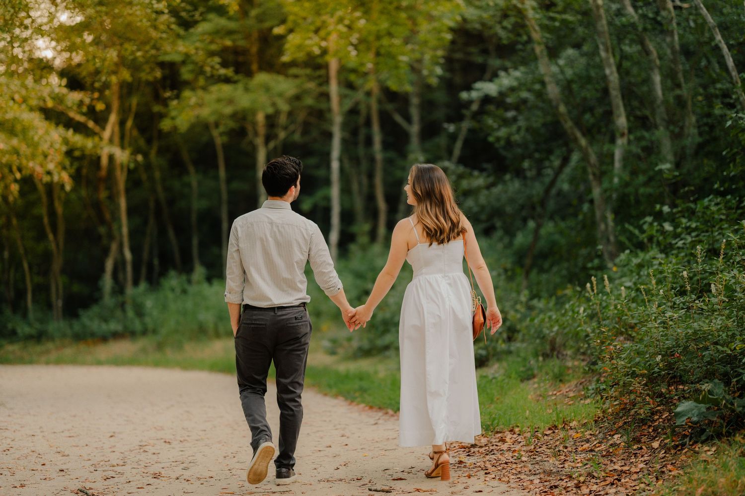 A loving couple walks together on a country path during golden hour as sunlight filters through autumn trees.