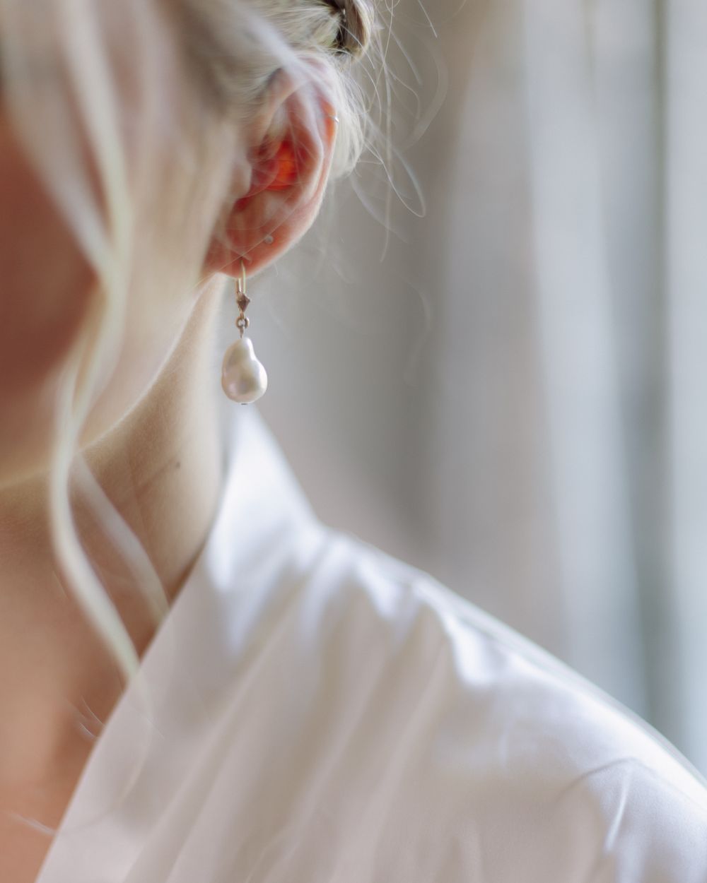 Close-up view of a pearl drop earring and white fabric with soft natural lighting.