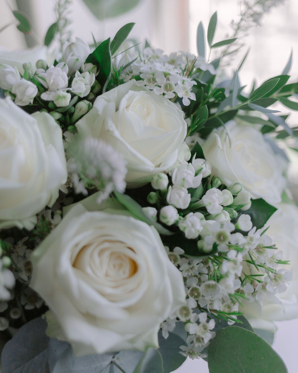 A romantic bouquet of white roses and baby's breath flowers with green foliage arranged in a soft, elegant composition.