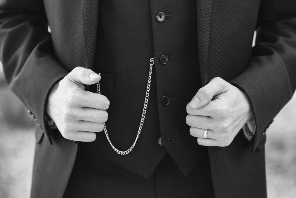 Detail shot of hands holding pocket watch chain against dark formal vest.
