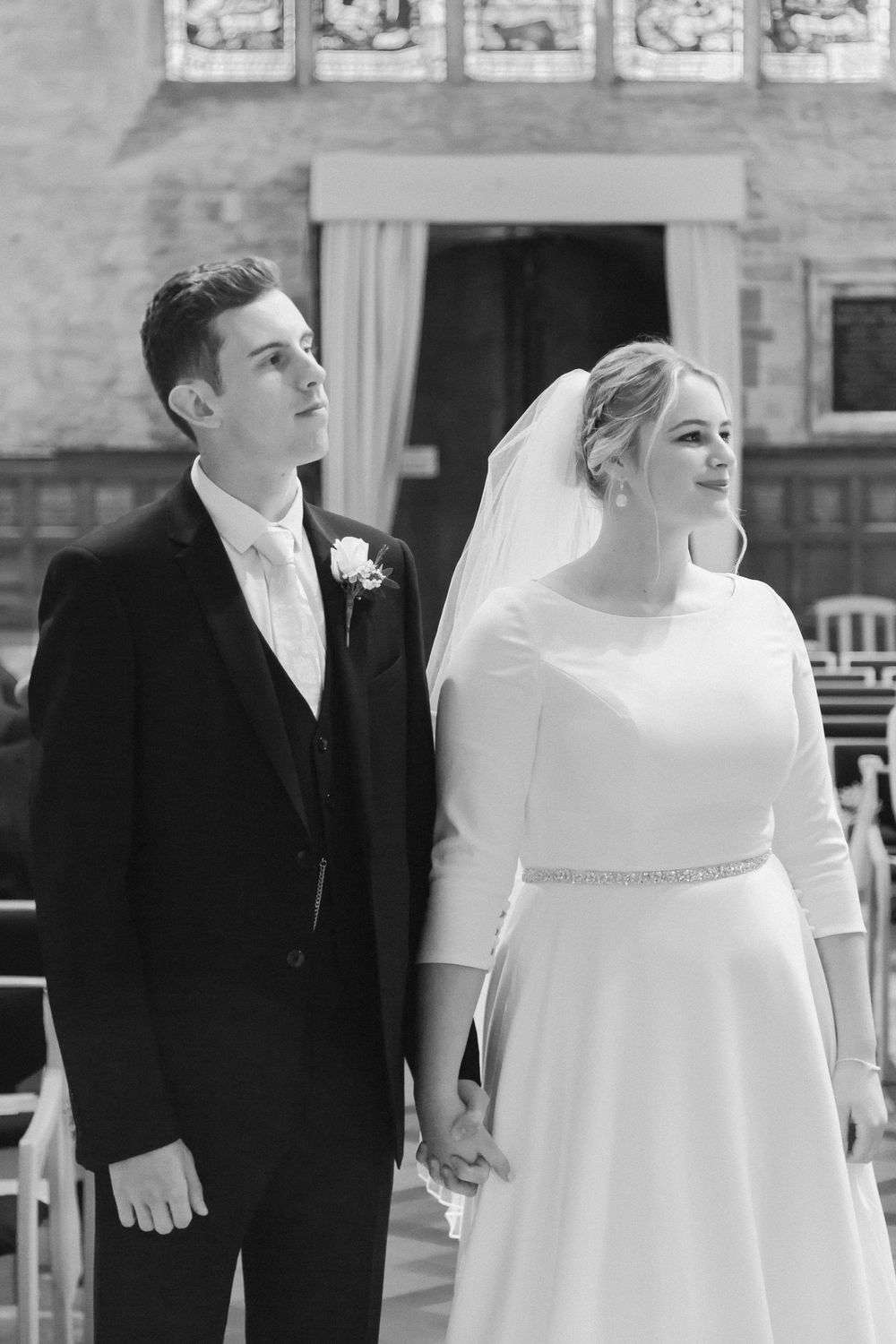 Elegant black and white wedding photograph showing a bride in a classic white dress and groom in tuxedo during ceremony.