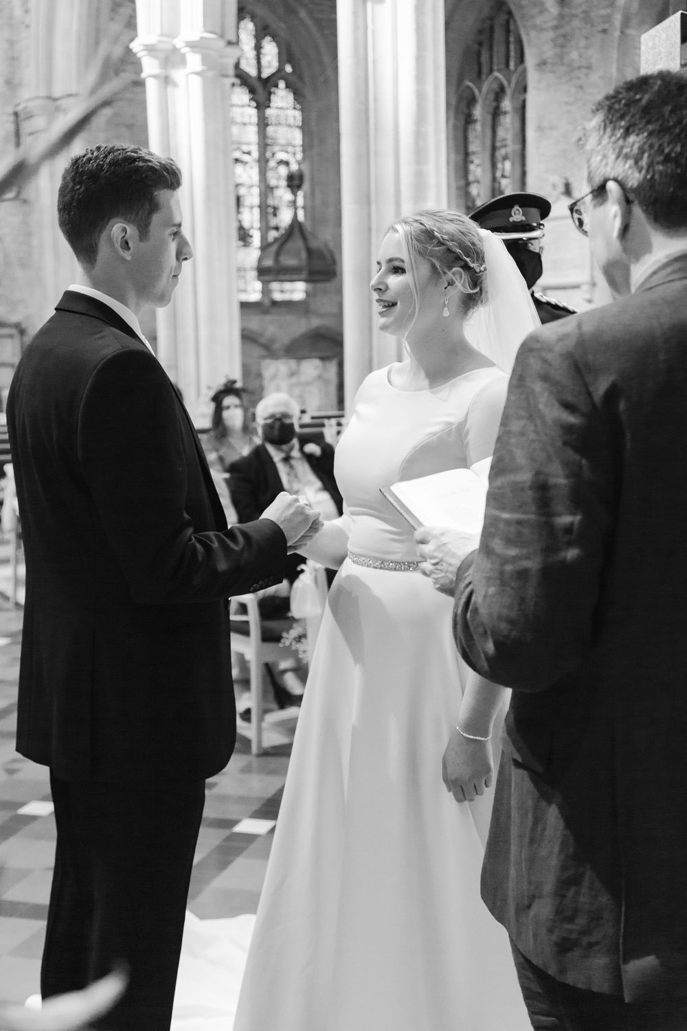 Black and white wedding ceremony photo showing a bride and groom exchanging vows at a traditional church altar.
