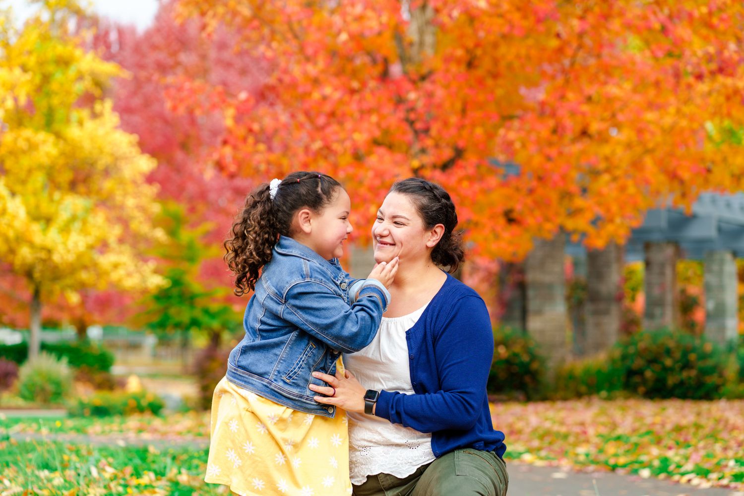 Mom and daughter share a moment with fall trees behind them at Reinhart Volunteer Park in Grants Pass, Oregon
