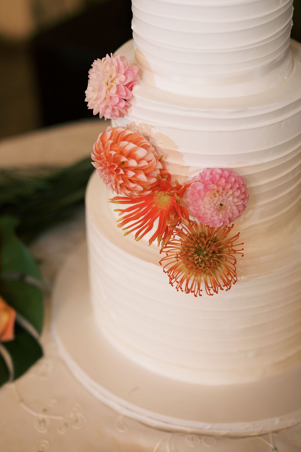 Elegant white wedding cake decorated with coral and pink gerbera daisies displayed in multiple angles.