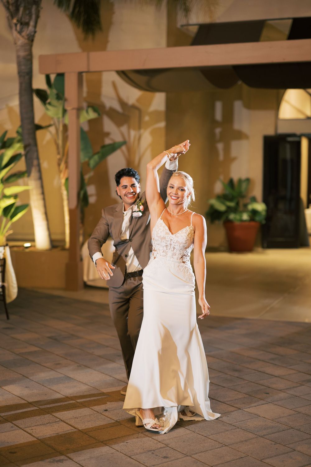 A festive wedding celebration featuring a couple dancing together on a tiled courtyard at night.