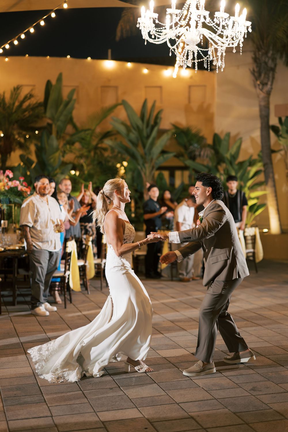 Wedding celebration with couple dancing under a crystal chandelier on an outdoor patio.