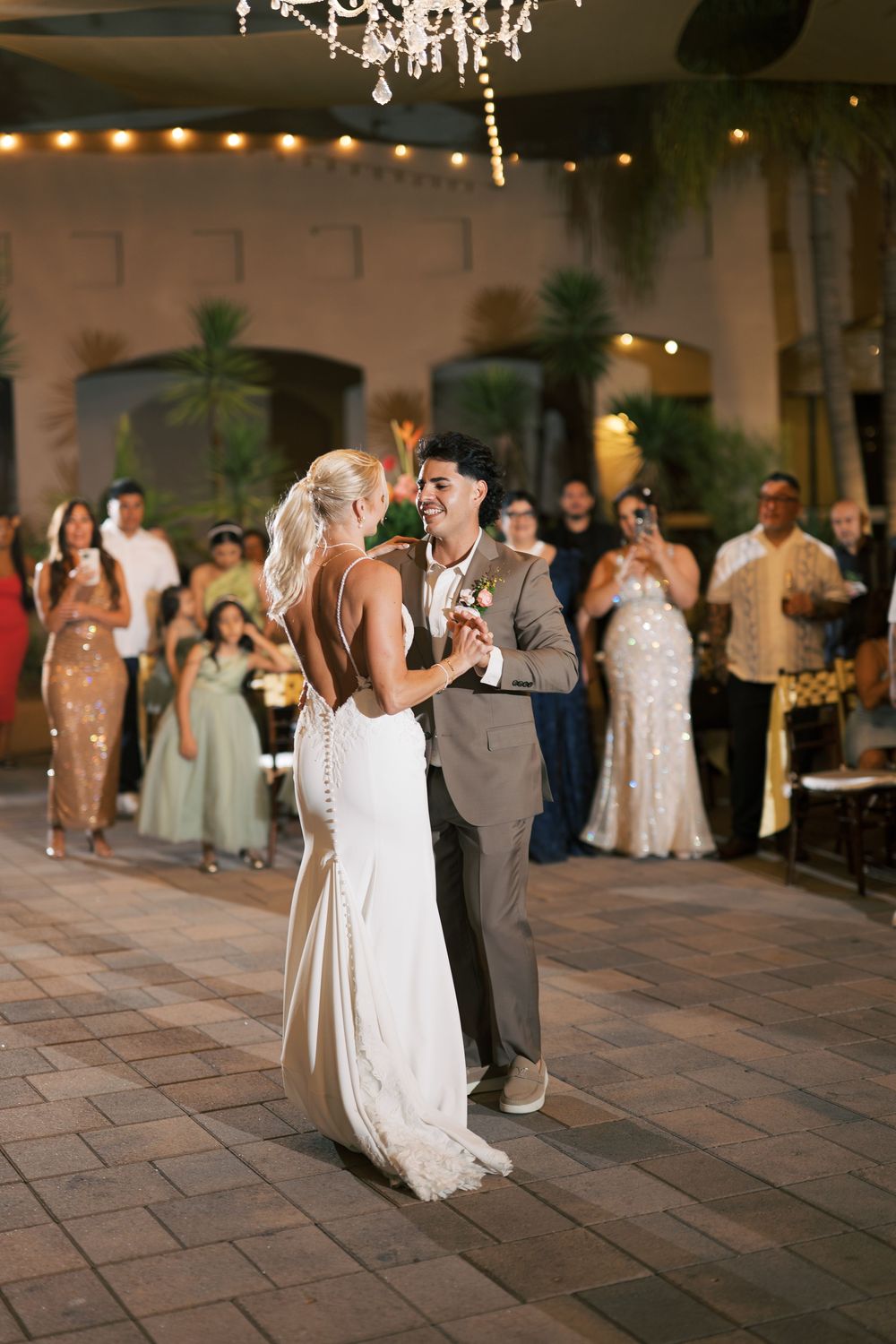 Couple sharing their first dance under a crystal chandelier at an elegant indoor reception.