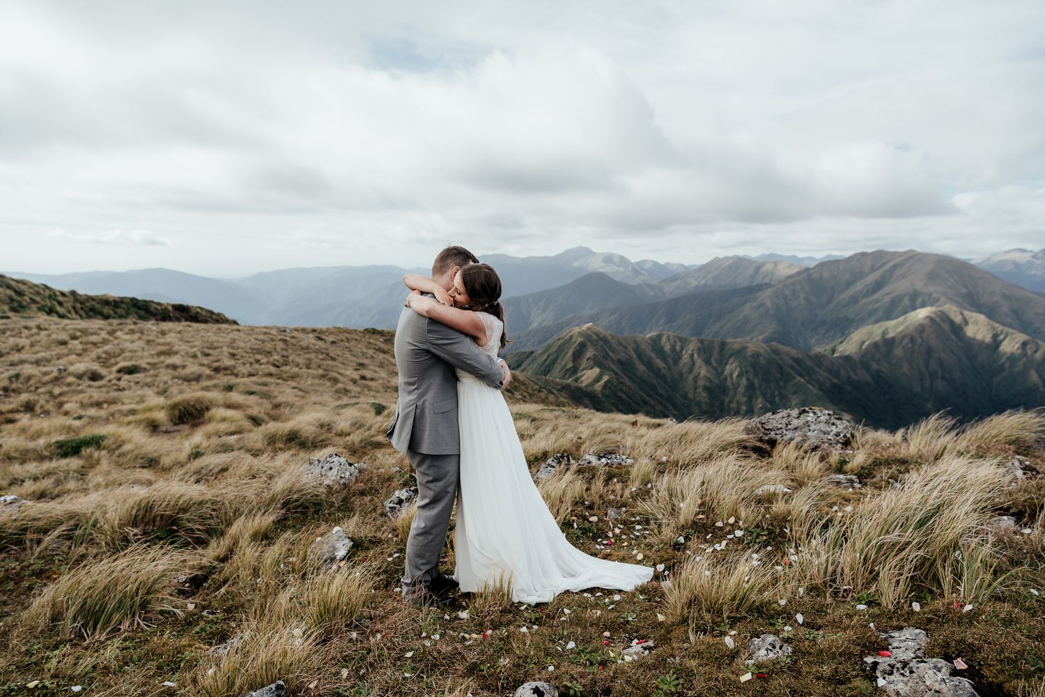 Couple embraces on the scenic Tararua Ranges Wairarapa with dramatic cloudy skies and rolling peaks in the distance by August and Vine