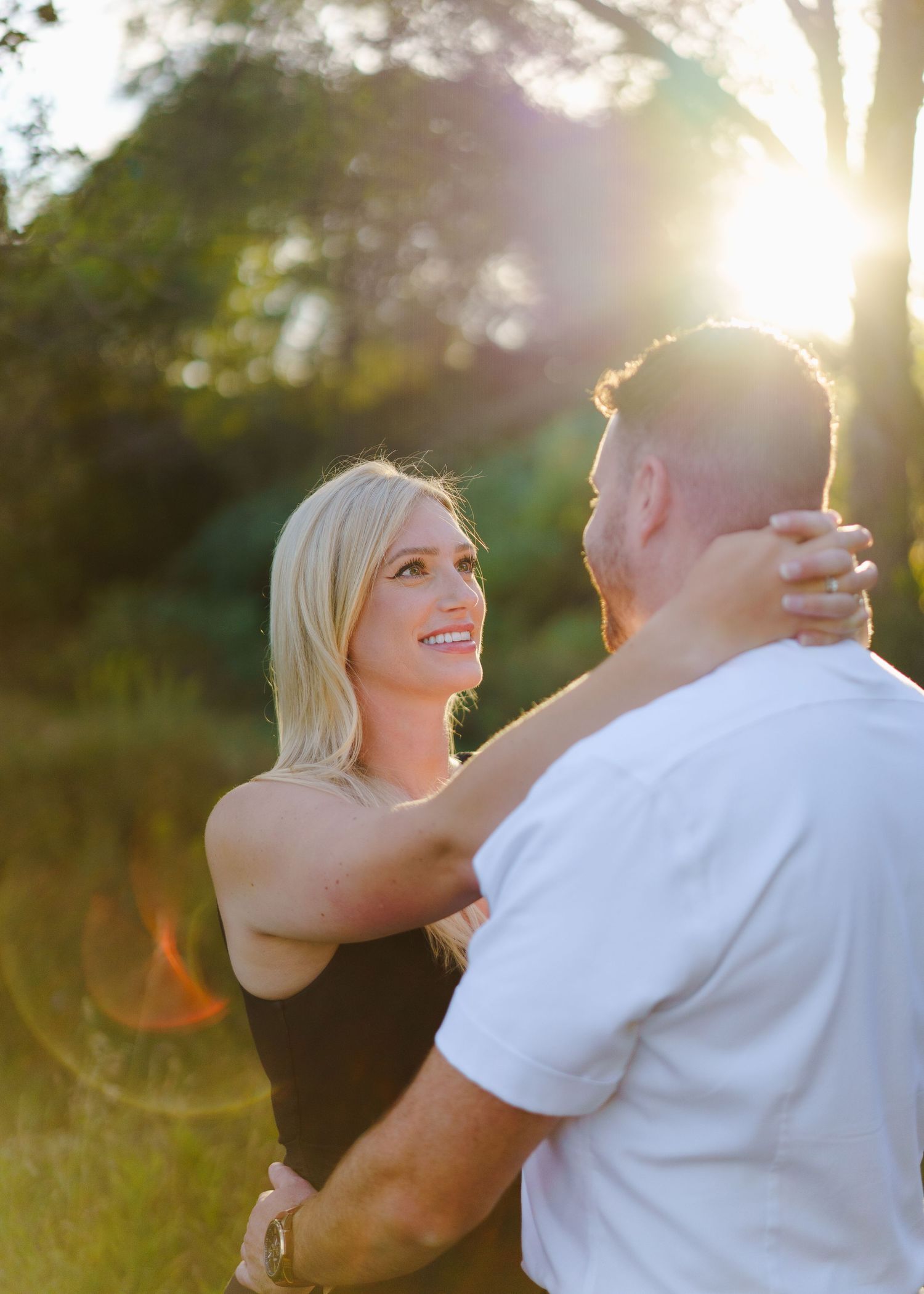 A couple embraces in a sun-drenched field during a romantic golden hour photoshoot.