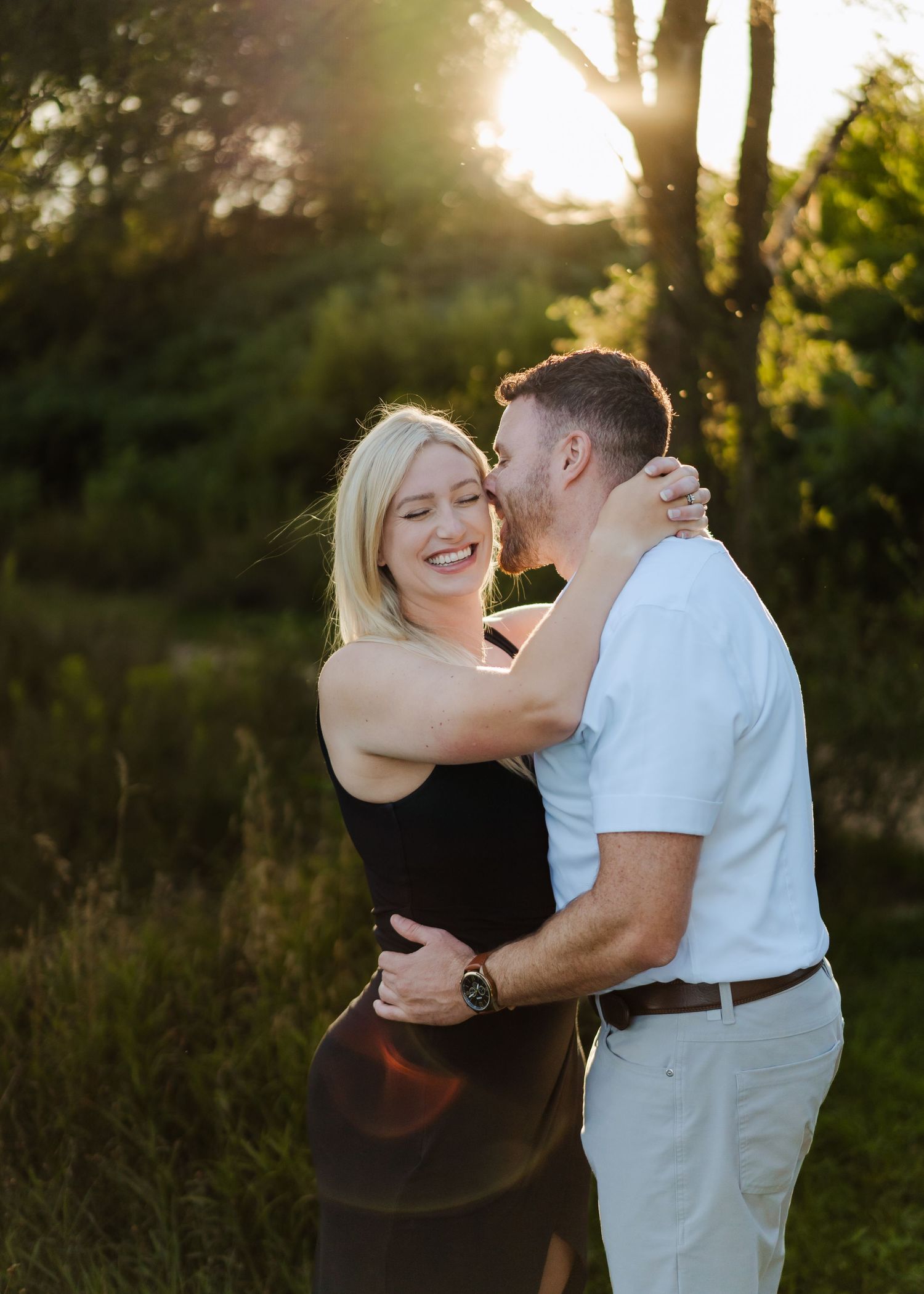 Romantic golden hour photoshoot of a couple embracing outdoors with sunlight filtering through trees.