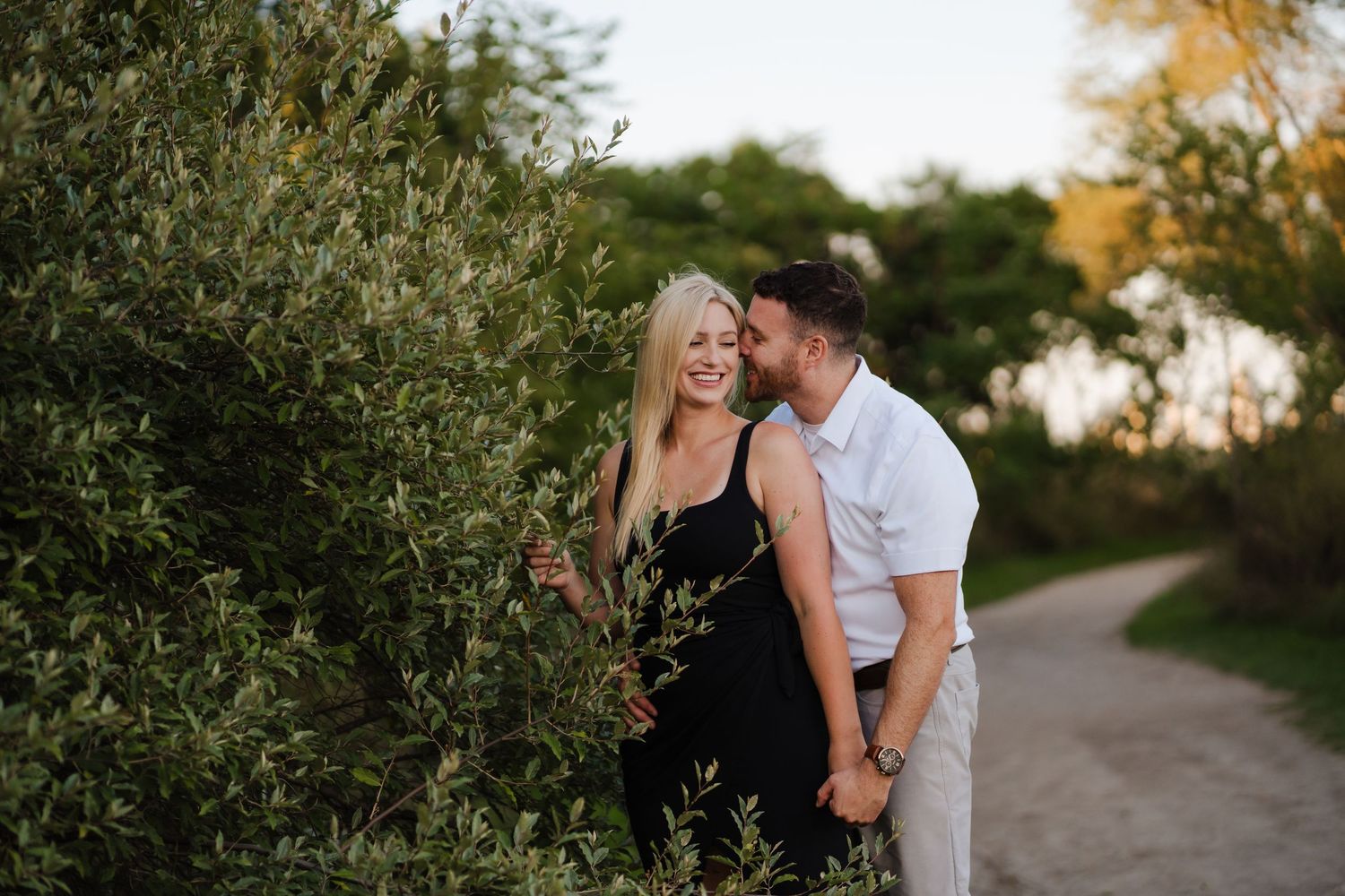A couple shares an intimate moment together along a tree-lined pathway during golden hour.