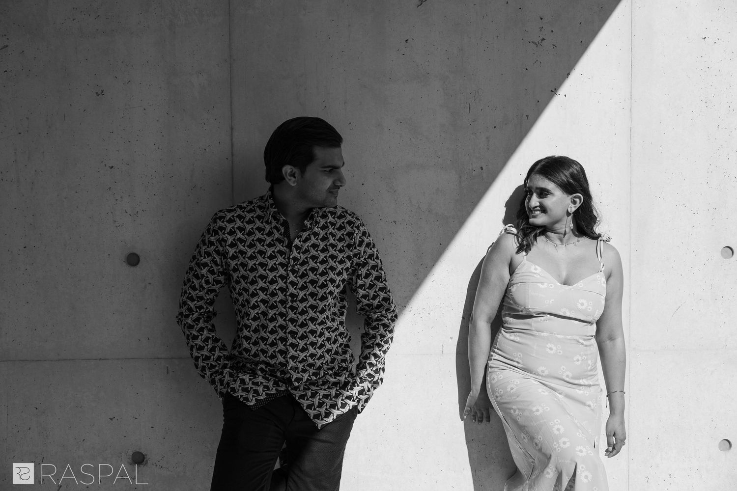 A couple poses against a concrete wall with dramatic lighting and shadows.