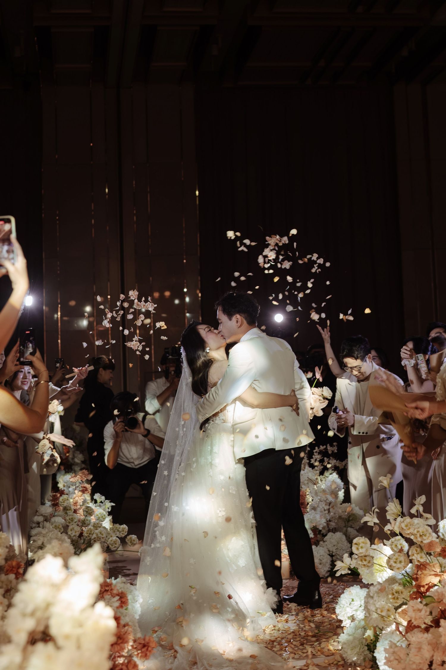 Bride and groom sharing first kiss at elegant wedding ceremony with floral confetti.