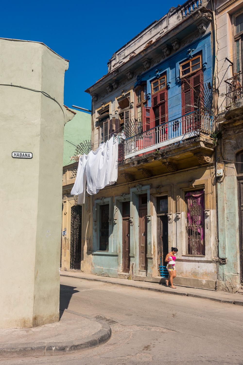 Weathered buildings with laundry hanging from balconies line a curving street in an old Cuban neighborhood.