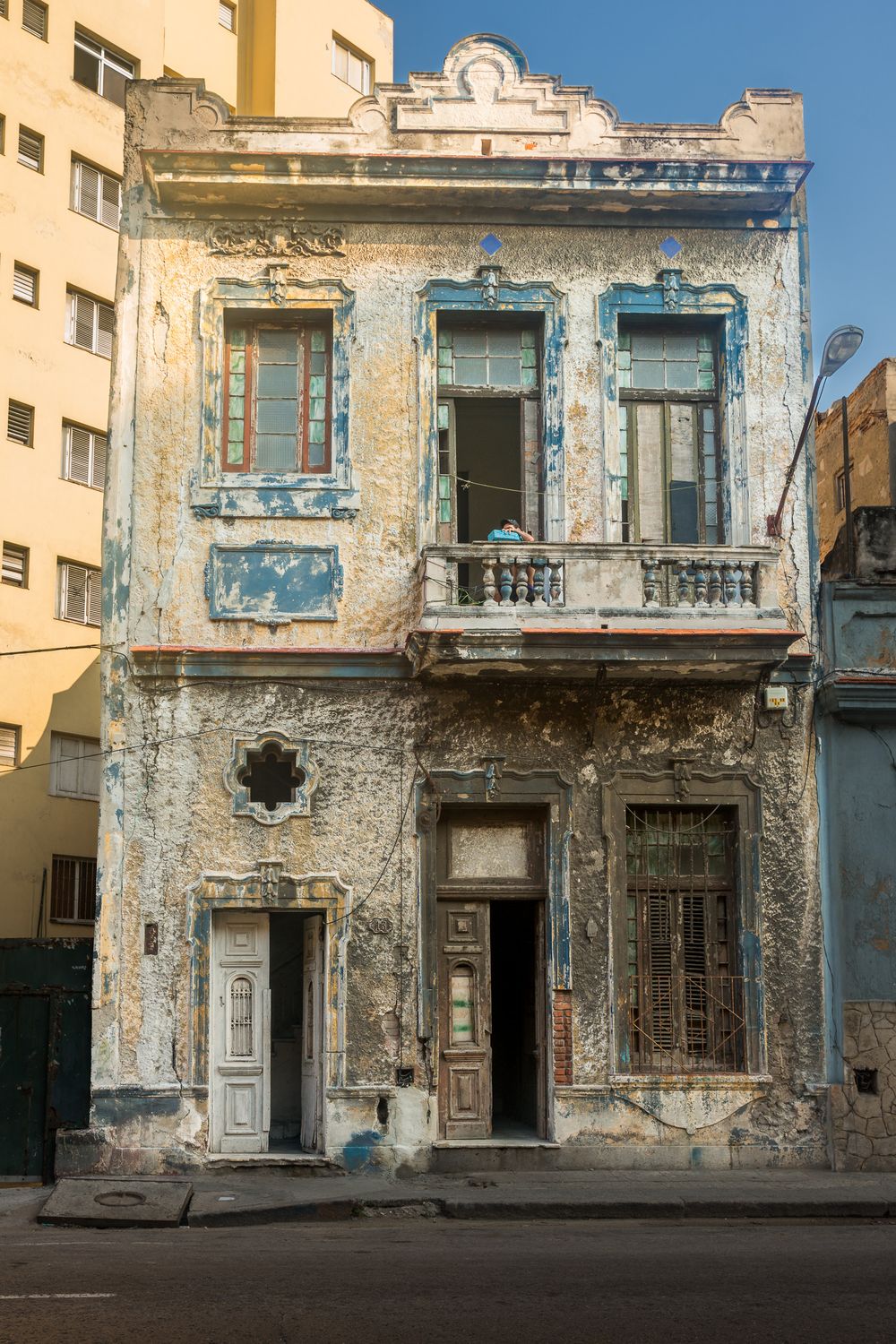 A dilapidated blue and cream colored building facade with crumbling walls and peeling paint in an urban setting.