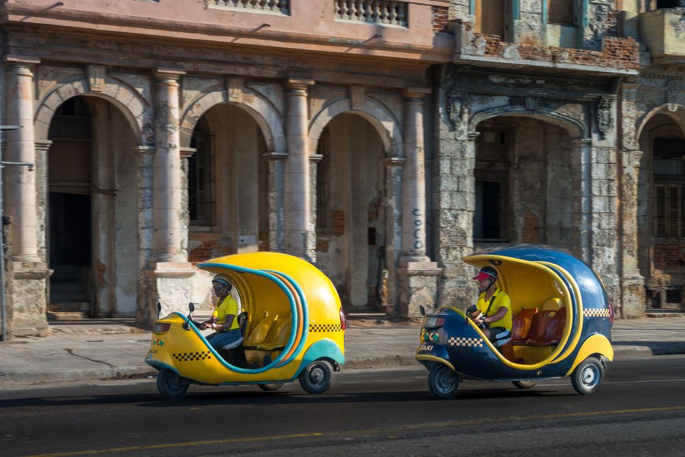 Colorful yellow and blue cocotaxis line up along a historic columned arcade in Havana, Cuba.