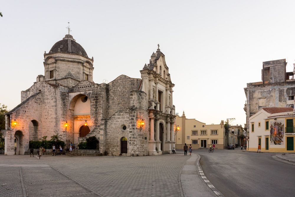 Panoramic view of historic stone buildings and churches in Ostuni, Italy, with illuminated archways at dusk.