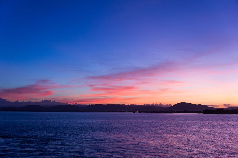 Collection of vibrant sunset and dusk scenes over calm ocean waters with mountain silhouettes.