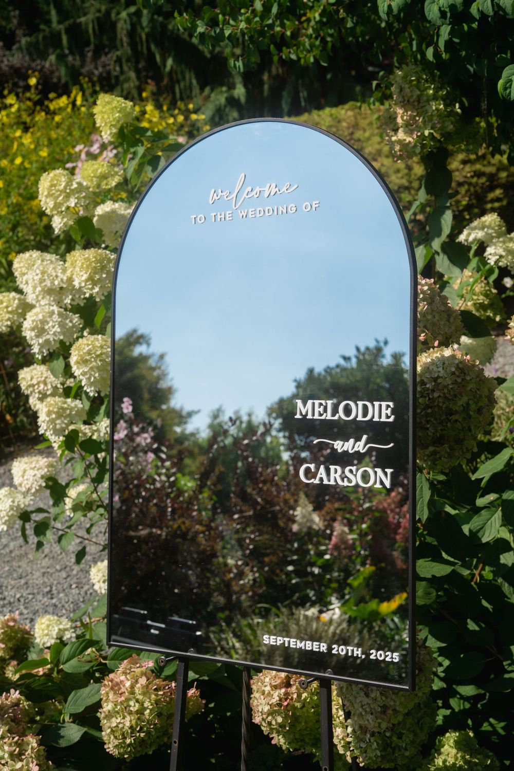 Elegant mirrored seating cards displayed among white hydrangea flowers at an outdoor wedding.