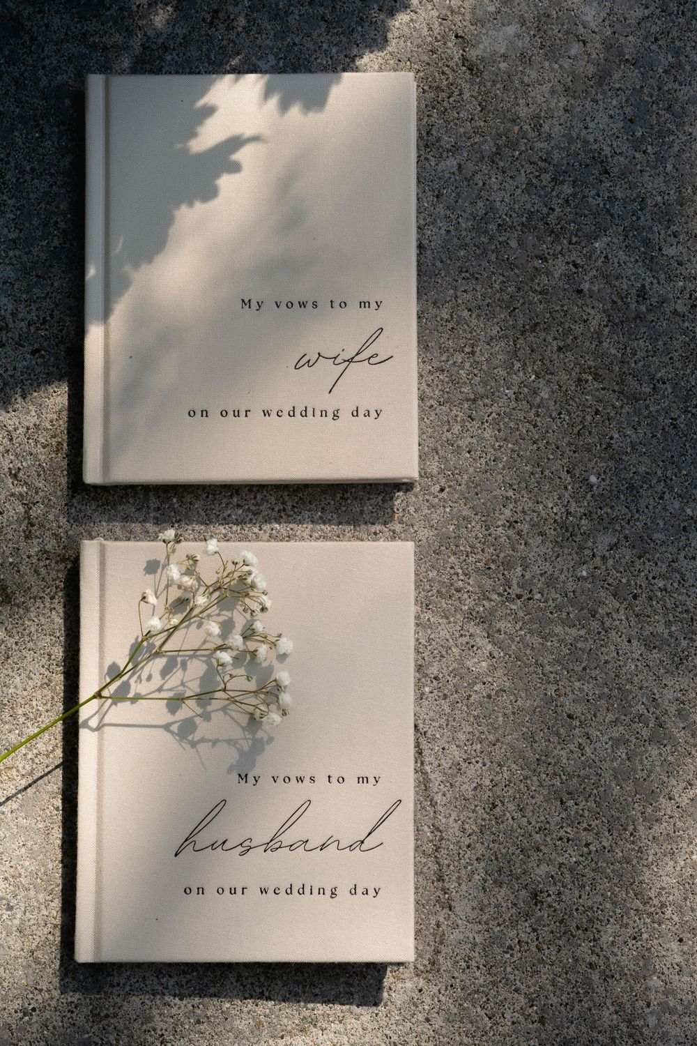Wedding vow books and albums with elegant calligraphy text lay arranged on a textured gray surface.