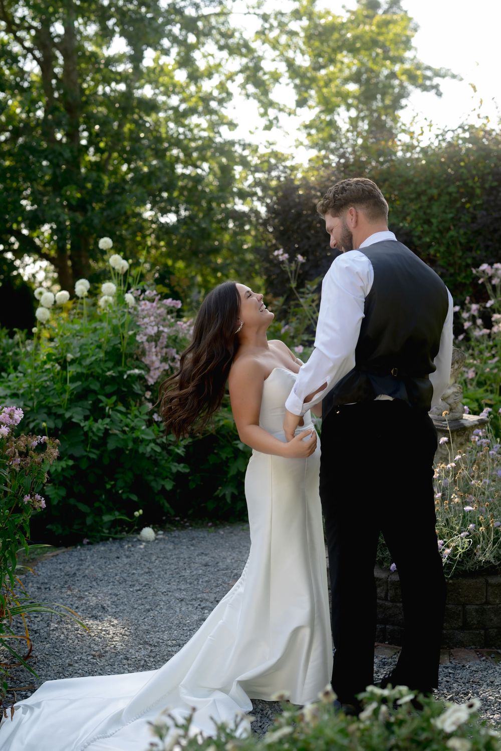 Romantic wedding couple embraces in a garden setting with blooming roses during golden hour sunset.