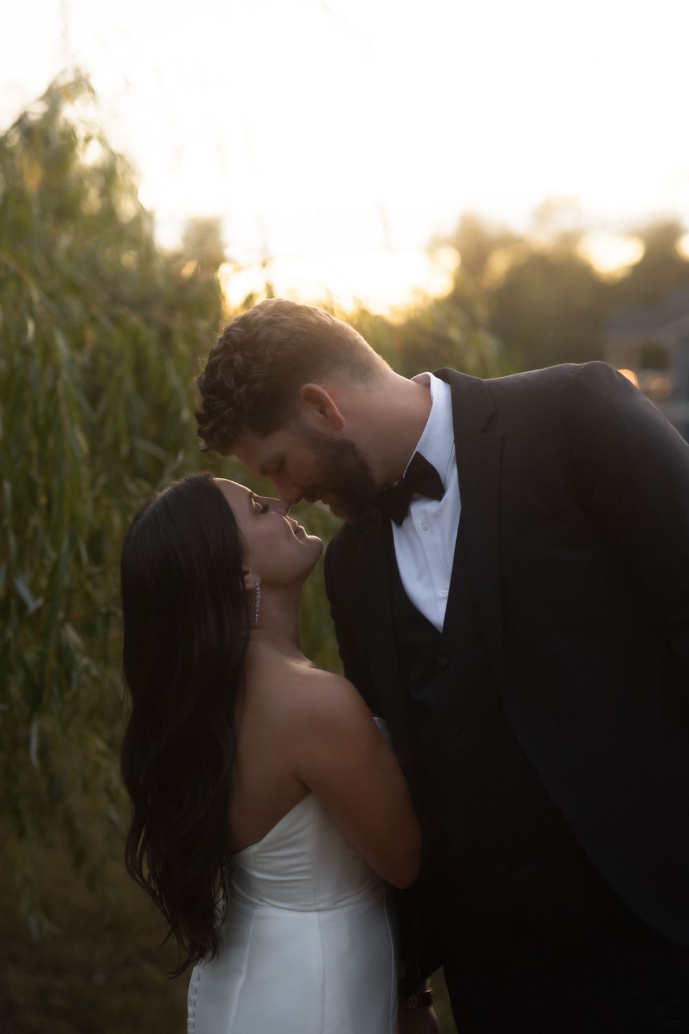 A romantic wedding couple shares intimate moments at sunset near a cornfield.