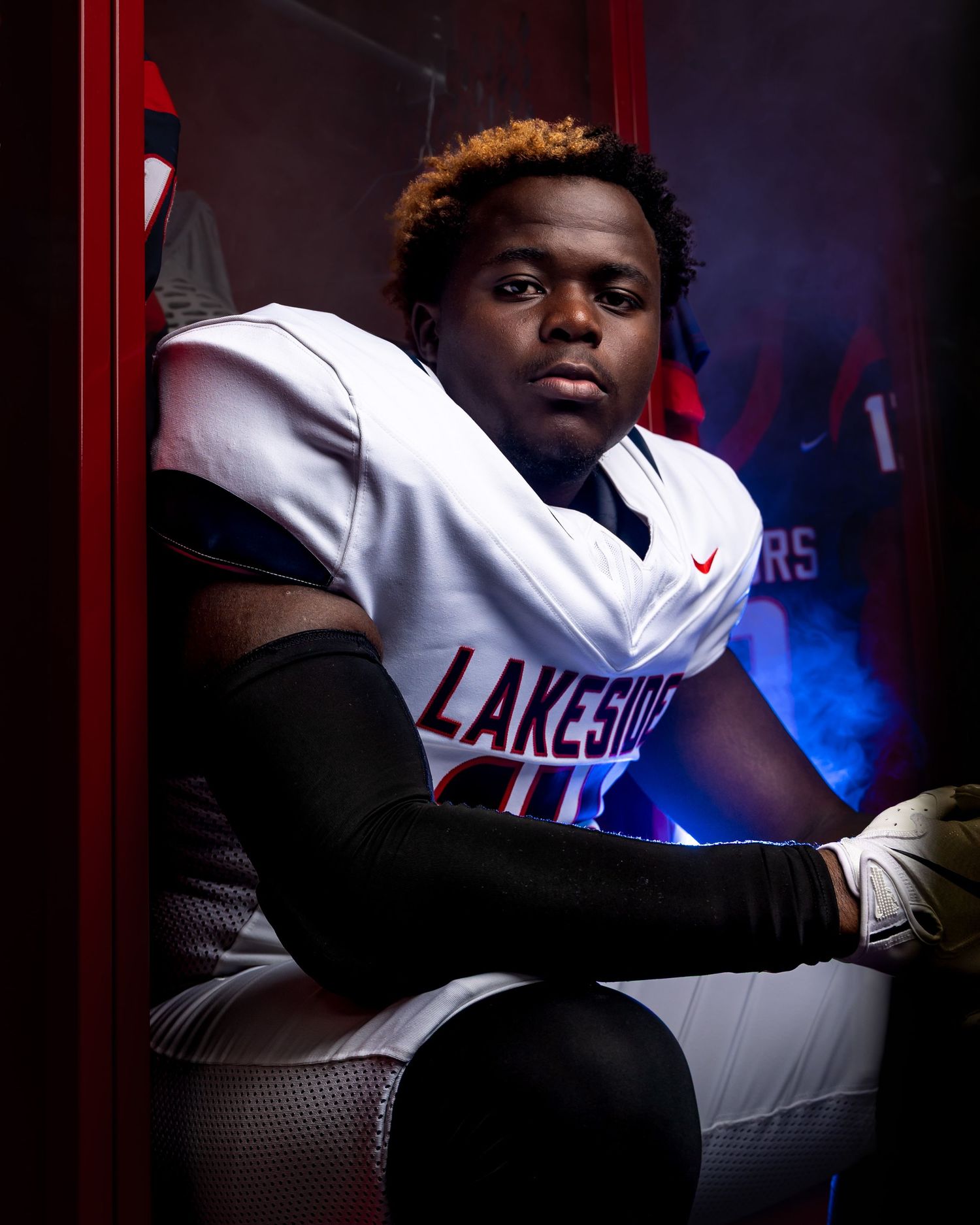 High school football player in white Lakeside uniform sits in dramatic lighting against dark background.