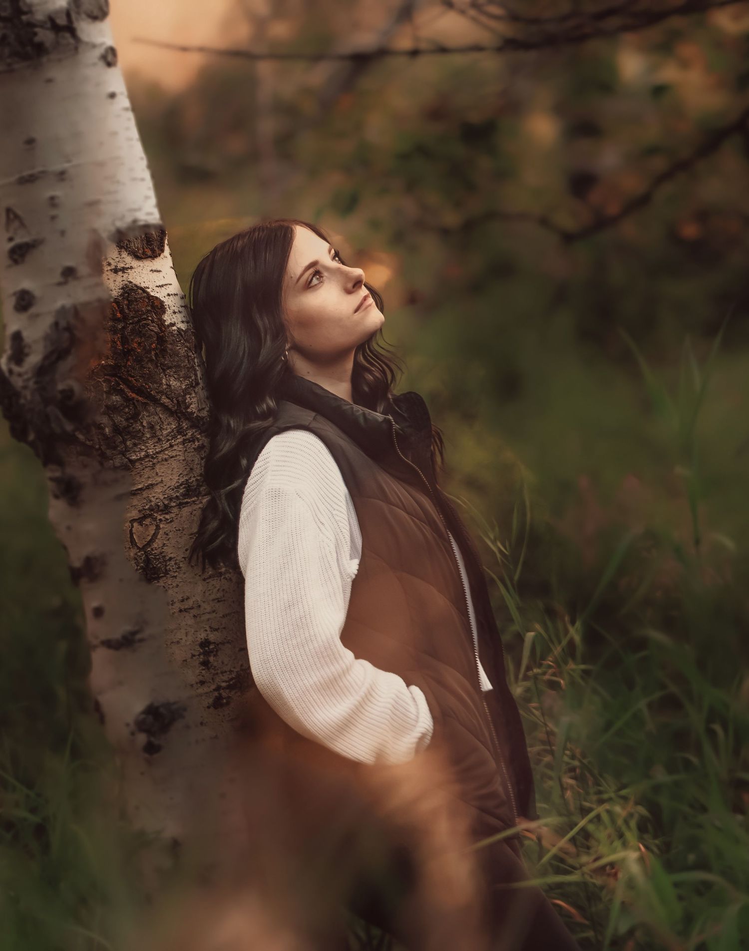 Person in a brown coat relaxing against a birch tree trunk in a forest during autumn.