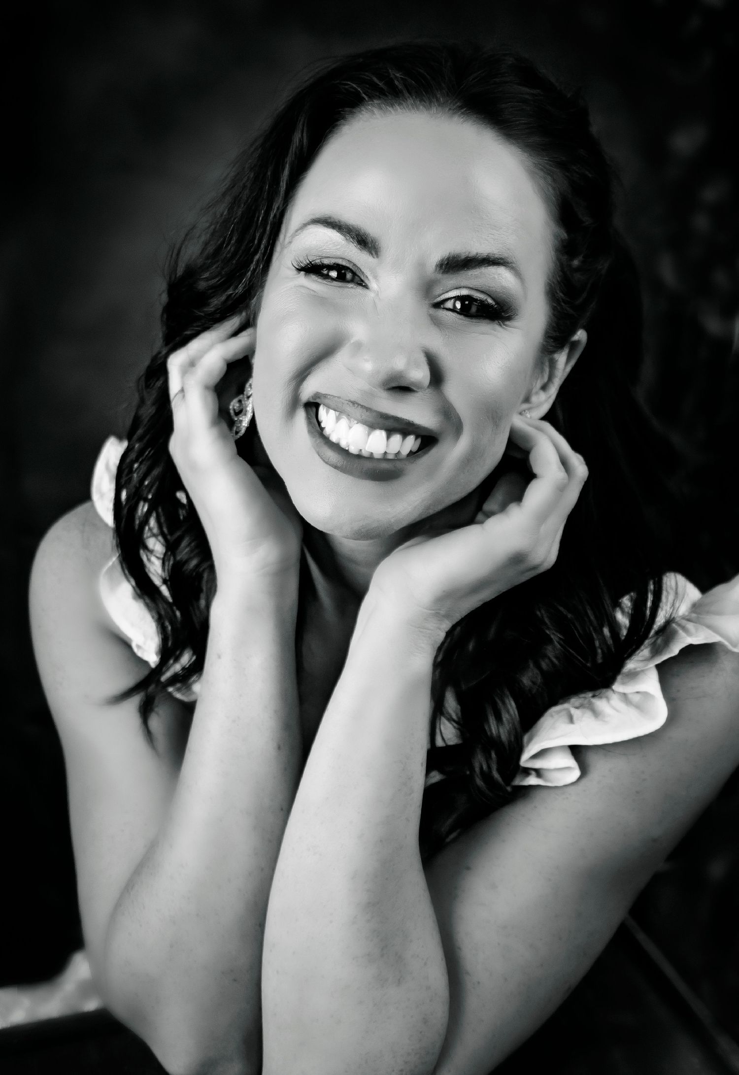 Black and white portrait with joyful expression and hands framing face.