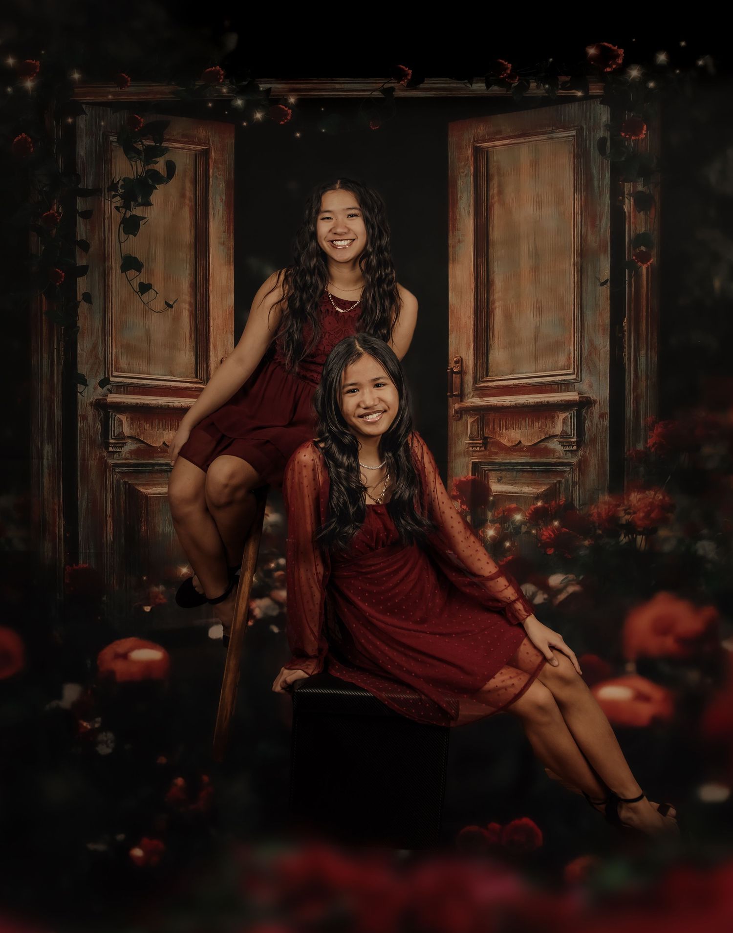 Moody portrait session with burgundy dress against dark vintage backdrop with scattered red rose petals.