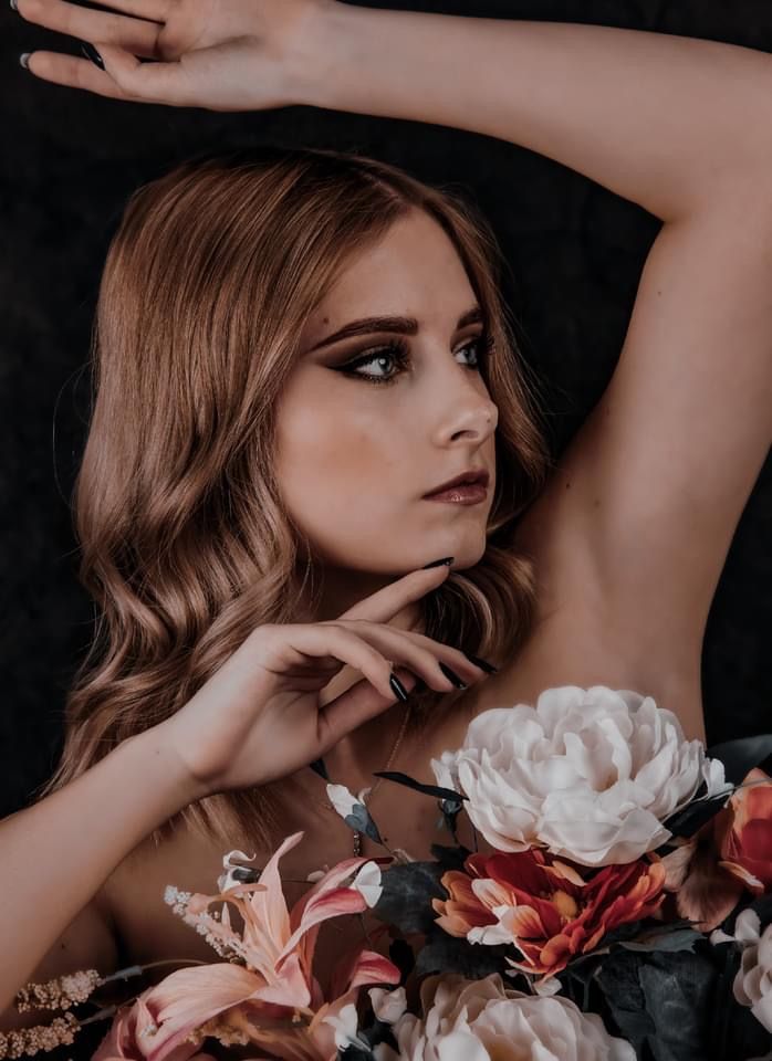 Dramatic fashion portrait with delicate flowers in muted tones against dark background creates ethereal artistic mood.