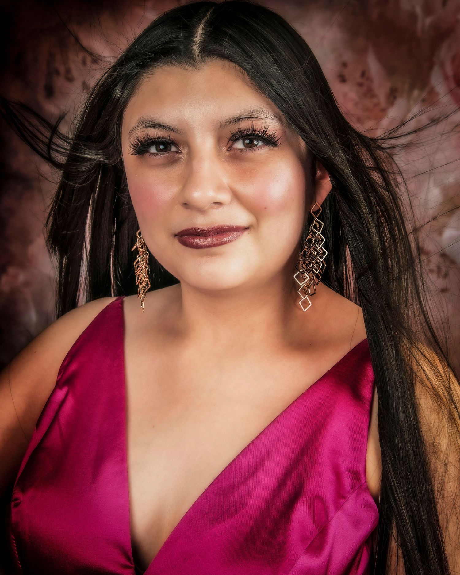 Glamorous portrait with dangling earrings and magenta dress against a dark background.