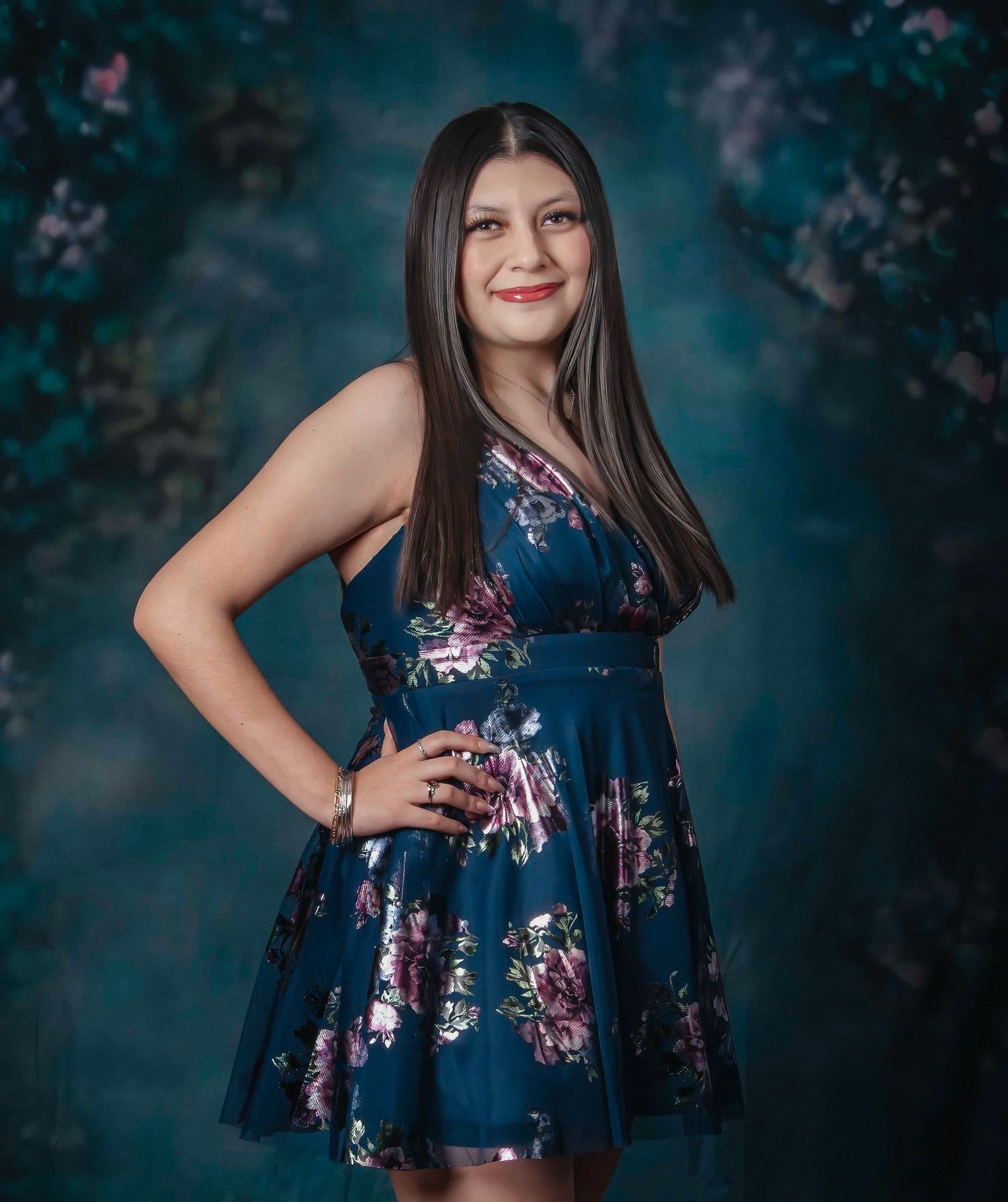 A person in a navy floral dress poses against a dark teal background with moody lighting.