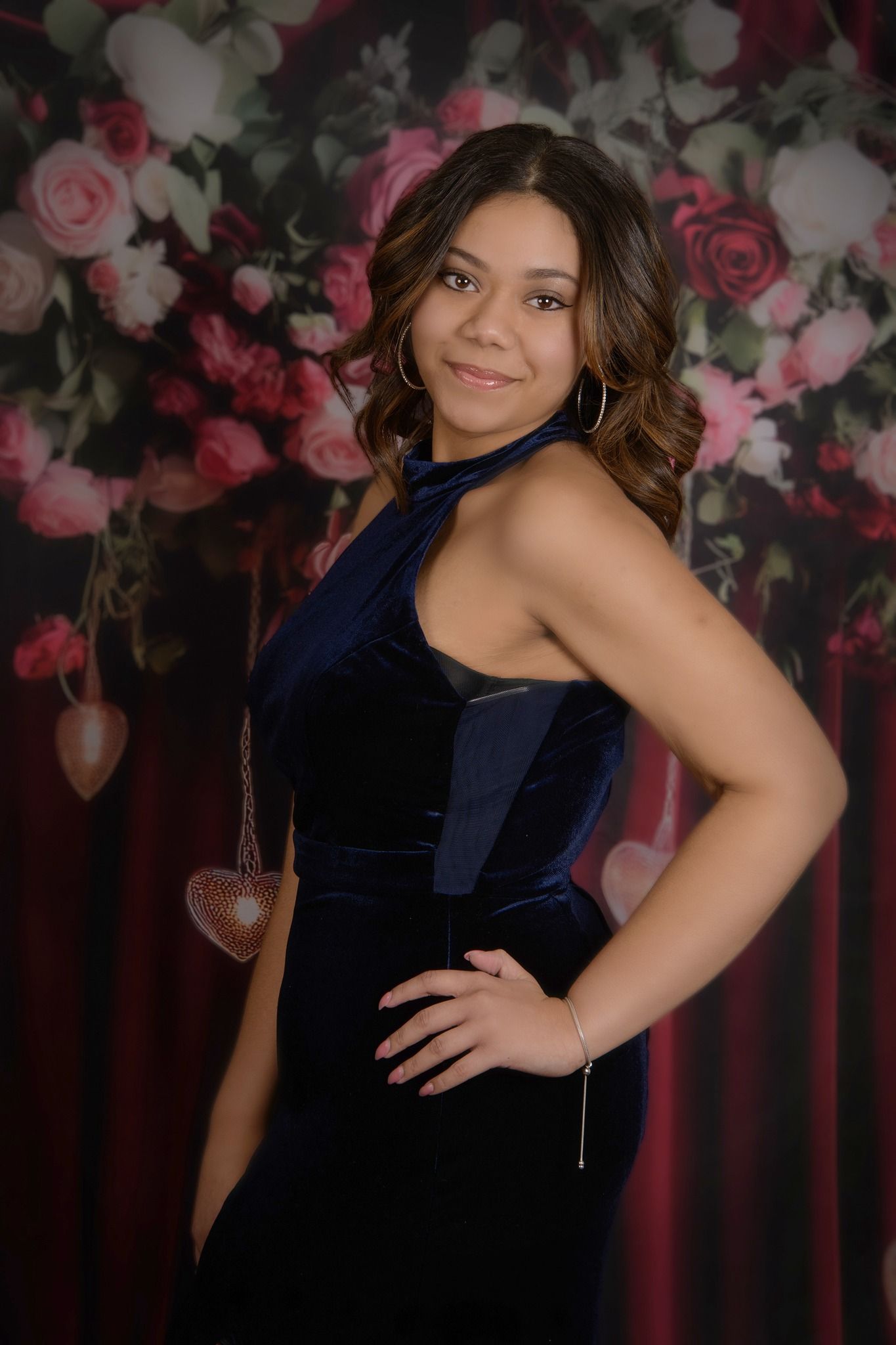 Studio portrait against floral backdrop featuring navy blue velvet dress in dramatic lighting.