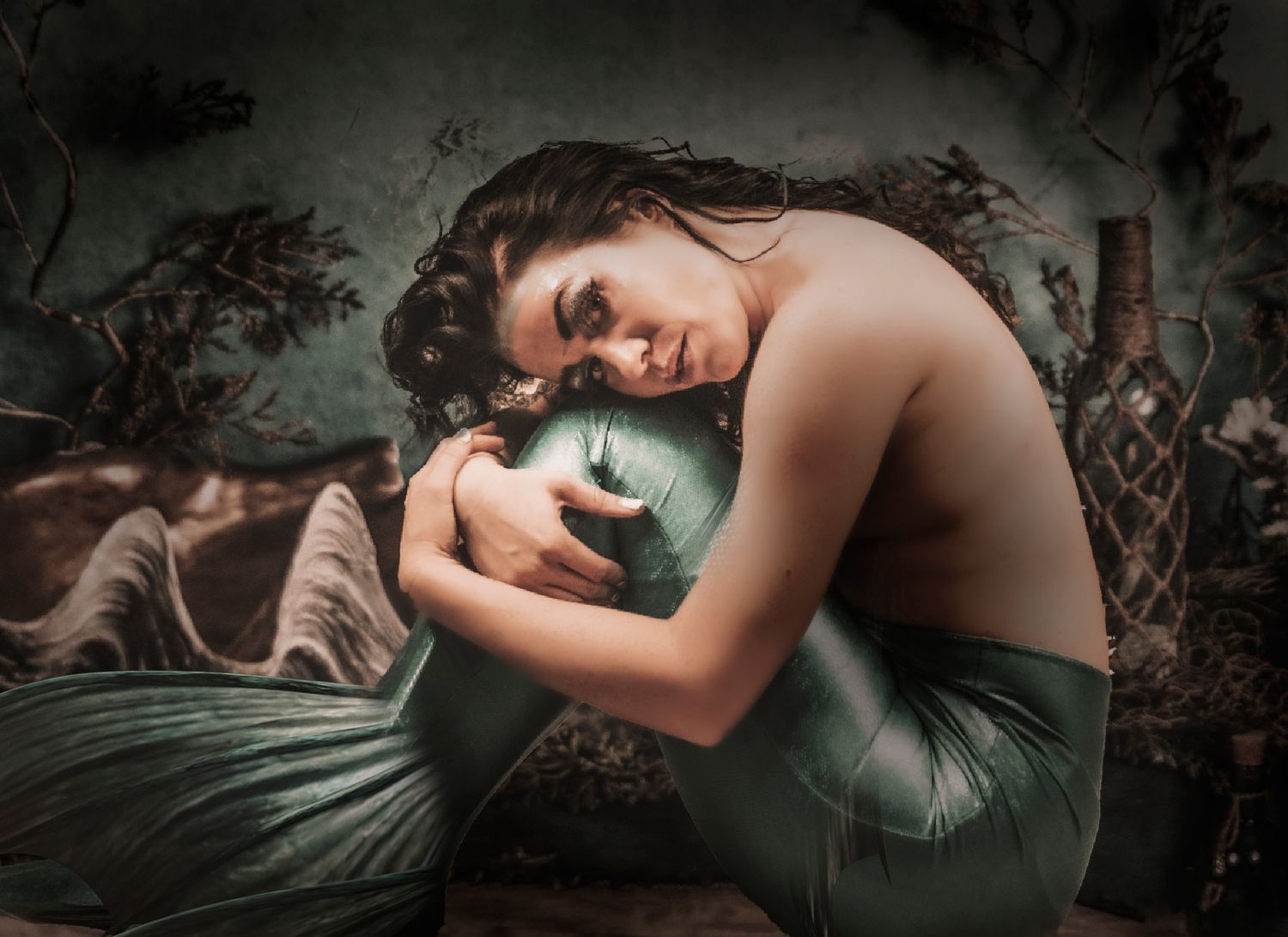Dark and moody boudoir photography featuring a person in elegant poses on green bedding.