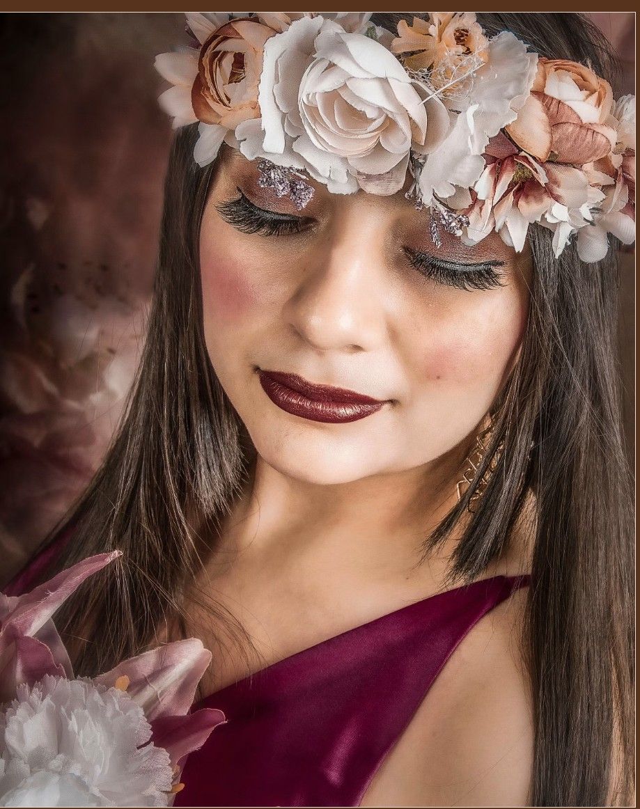 Close-up artistic portrait with soft pink floral decorations and burgundy dress creating a dreamy atmosphere.