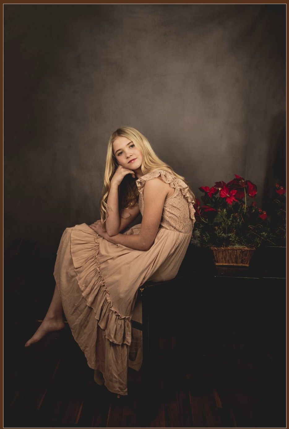 A figure in a flowing beige ruffled dress poses elegantly against a dark backdrop with red flowers in the scene.