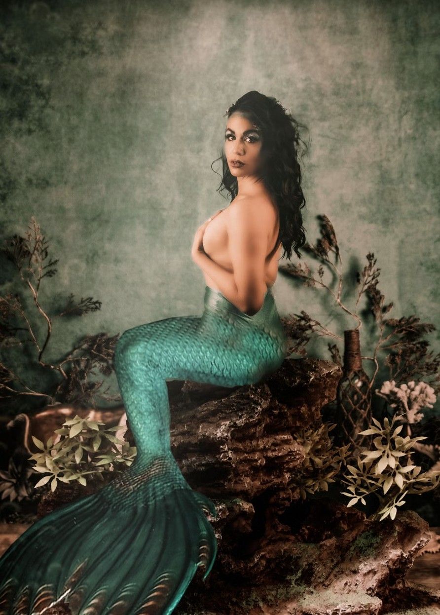 A mythical mermaid with a glittering turquoise tail poses against a moody textured backdrop with floral elements.