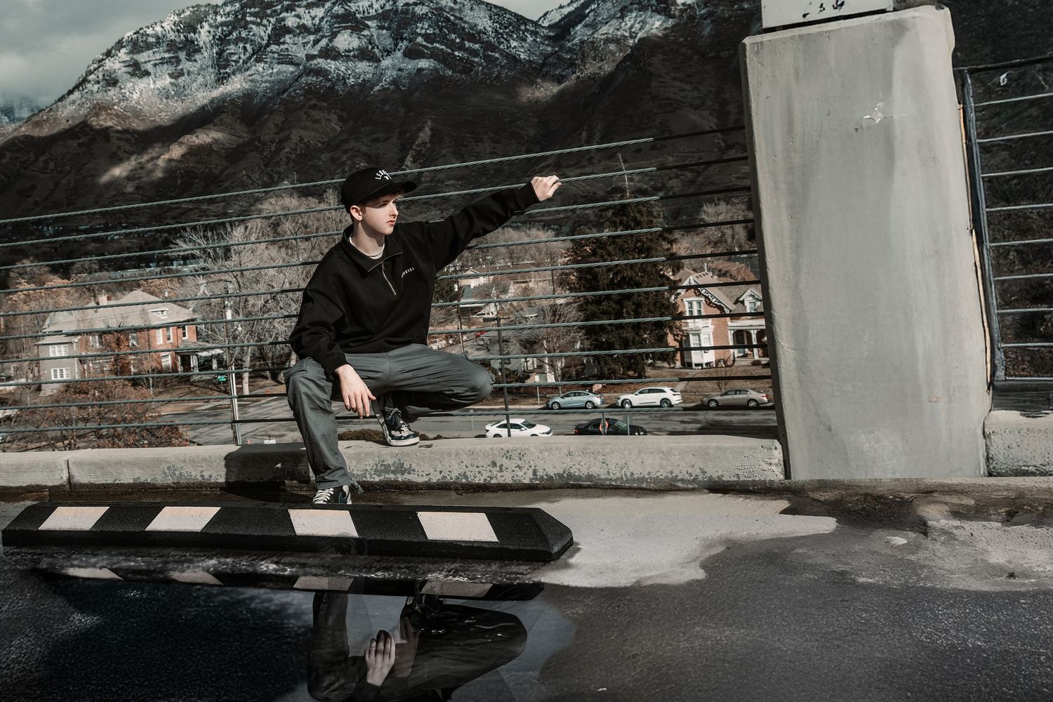 Skateboarder performs trick on rail against brick wall backdrop with snowy mountains in background.