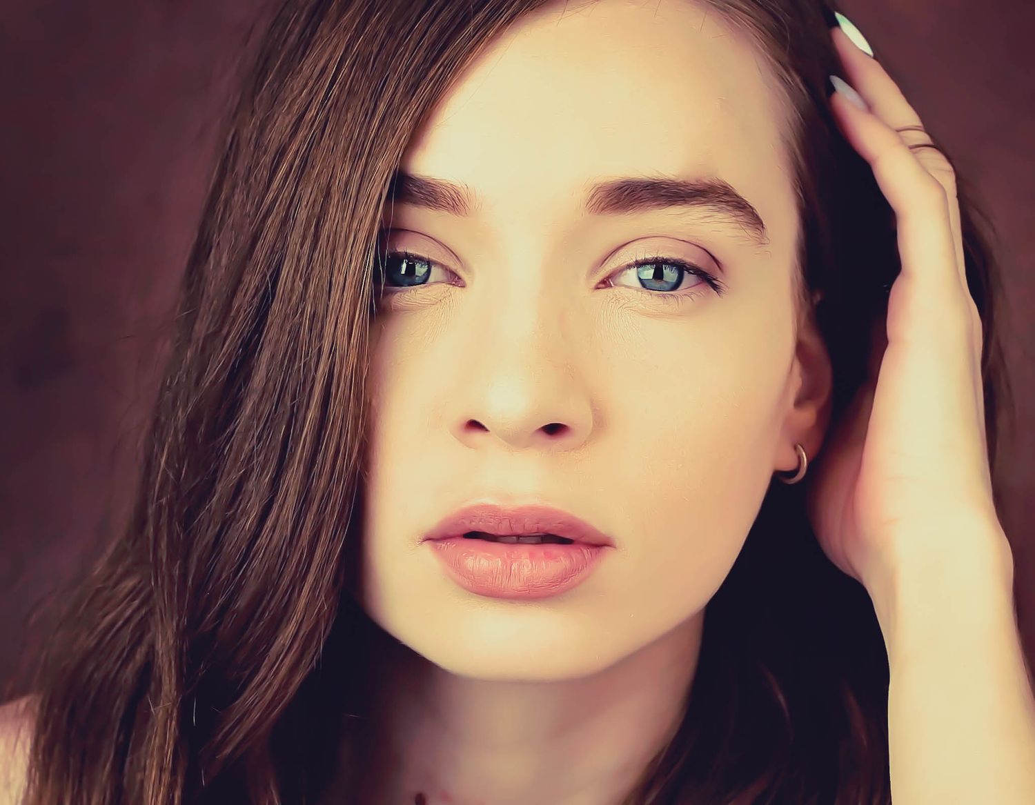 Artistic portrait with soft lighting showcasing natural beauty and hand placed in dark hair.