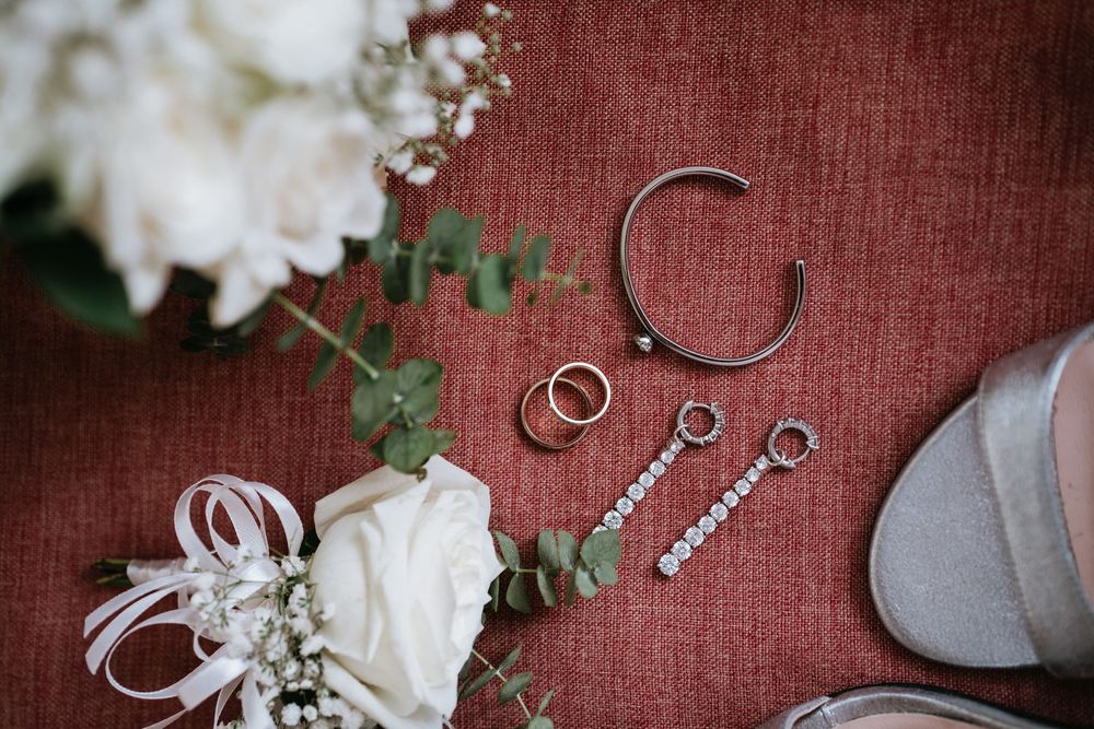 Wedding accessories including rings and floral elements arranged on a burgundy textile background.