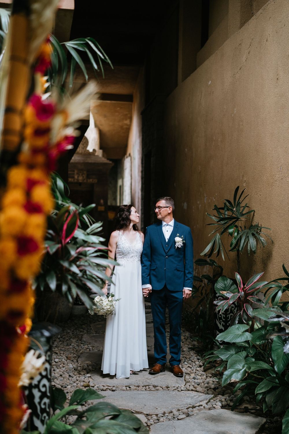 An intimate wedding moment photographed in a garden walkway with tropical plants and stone path.
