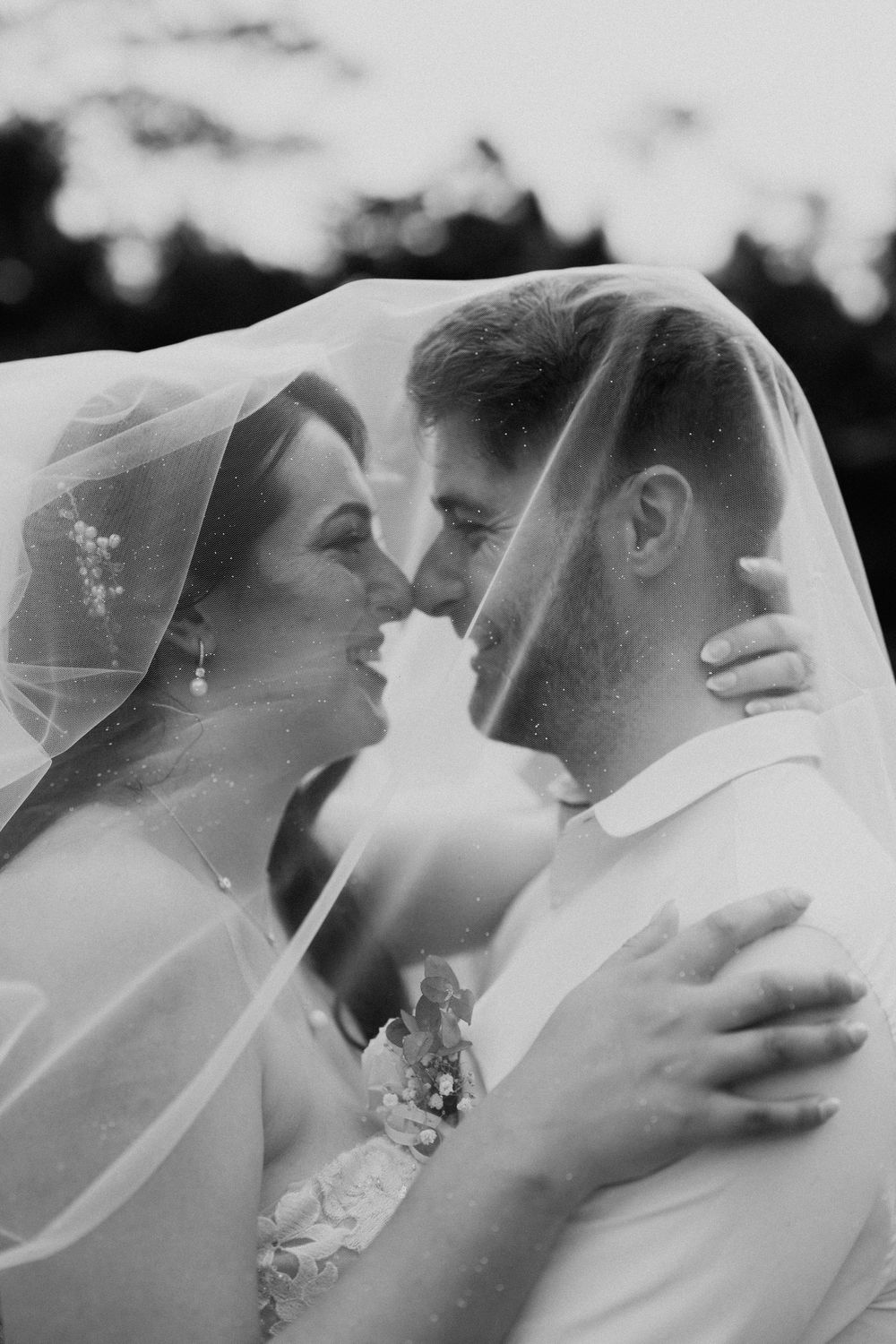 Intimate black and white portrait of newlyweds sharing a tender moment under a sheer veil.