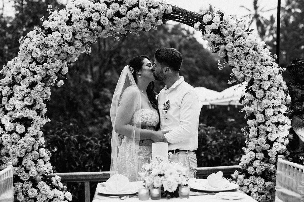 Wedding ceremony under an elegant white floral arch with romantic garden backdrop.